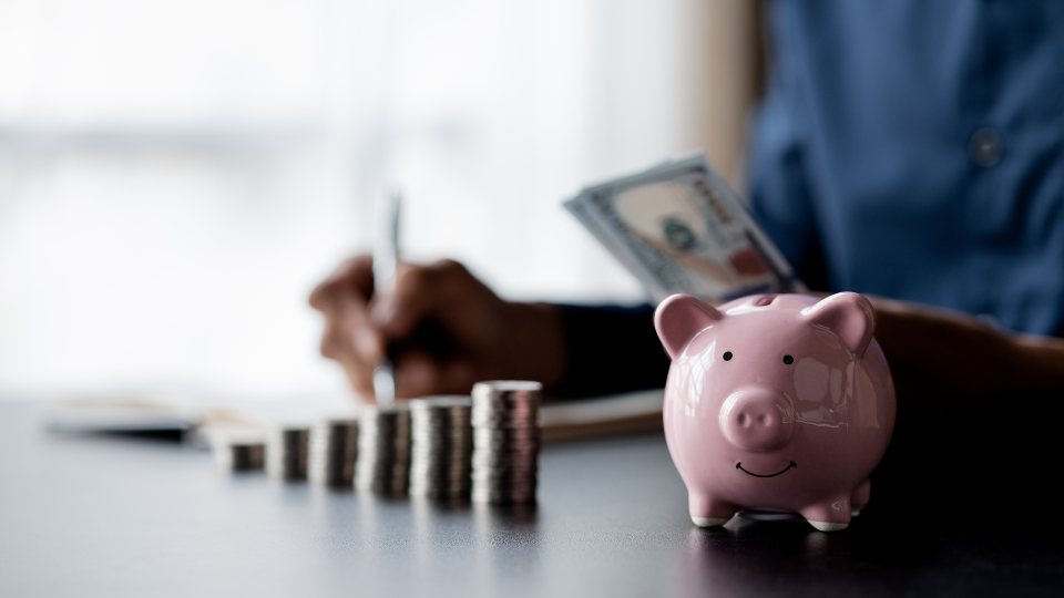 Person counting money with a stack of coins and piggy bank