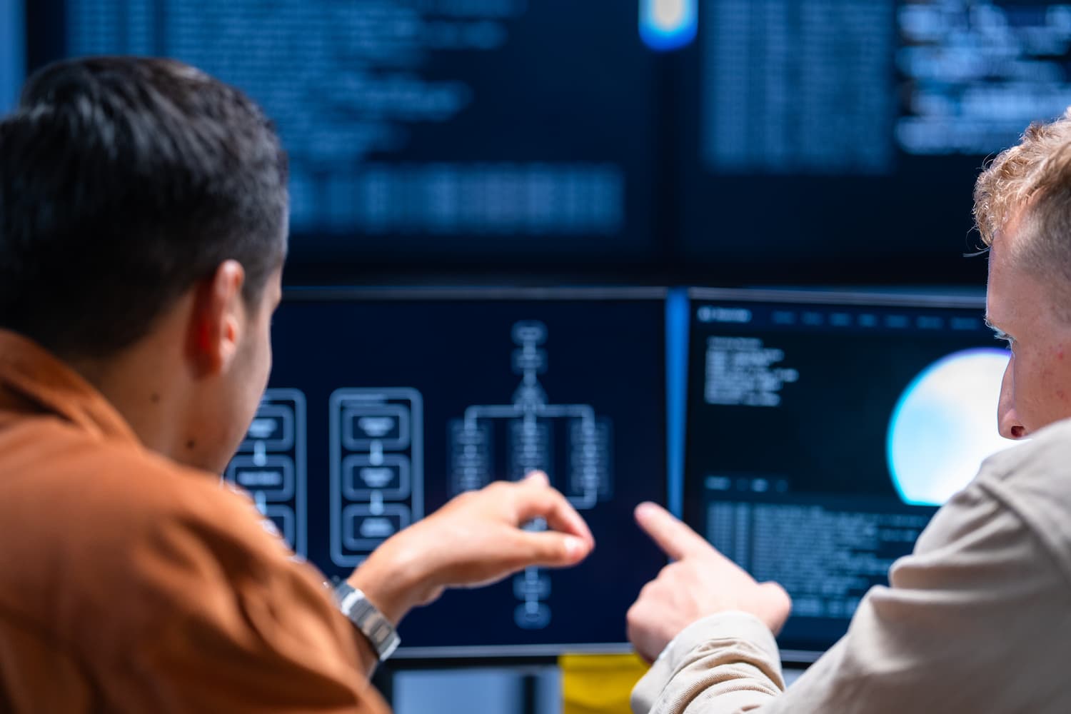 Cybersecurity professionals reviewing network diagrams and system data on multiple computer monitors.